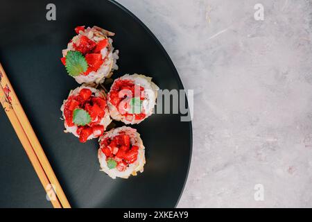 Fusion-Sushi-Rolle mit Erdbeerbelag auf dunklem Teller mit Essstäbchen, elegante Portion Stockfoto