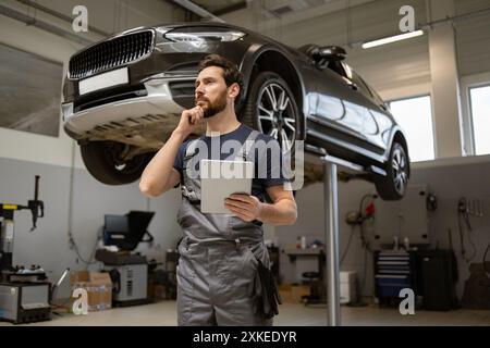 Mechaniker, der in der Garage Autoreparaturarbeiten mit einem Tablet überprüft Stockfoto