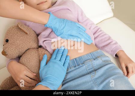 Männlicher Kinderarzt untersucht den Bauch des kleinen Mädchens auf der Couch in der Klinik, Nahaufnahme Stockfoto