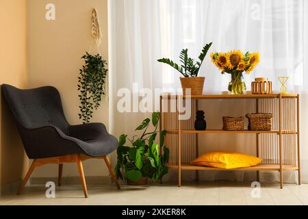 Vase mit schönen Sonnenblumen und Zimmerpflanzen auf einem Regal in der Nähe des Sessels im Zimmer Stockfoto