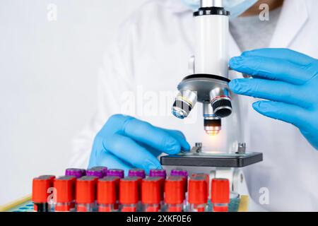 Arzt Hand nimmt ein Blutprobenröhrchen aus einem Rack mit Maschinen der Analyse im Labor Hintergrund, Techniker hält Blutprobentest in der Forschung Stockfoto