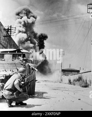 Leghorn, Italien, 7. August 1944 in Deckung, CPL Duane T. Moen, Minneapolis, Minn, ist auf der Suche nach Scharfschützen, als seine fünften Armeekumpels in einer der Hauptstraßen, die zum Hafen von Leghorn führen, Minen absetzten. Eine riesige Rauchsäule steigt im Hintergrund auf, während die Minen explodieren. Stockfoto