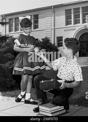 Usa c. 1952 Ein kleiner Junge bietet einer Klassenkameradin eine Orange aus seiner Brotdose. Stockfoto