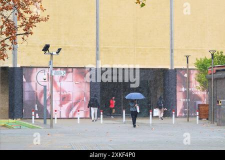 Menschen, die im Winter im Regen vor der Kunstgalerie laufen, eine mit Sonnenschirm, im Perth Cultural Centre in Northbridge, Perth, Western Australia. Stockfoto