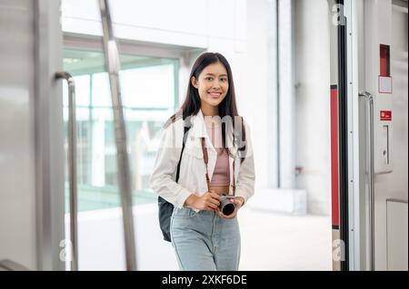 Eine schöne, positive junge asiatische Reisende mit Rucksack und Kamera steigt in einen Skytrain oder eine U-Bahn und pendelt uns in einer Stadt Stockfoto