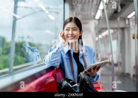 Eine schöne junge asiatische Passagierin träumt tagträumen und blickt auf den Blick nach draußen, während sie ihr digitales Tablet in einem Himmelszug benutzt und im C pendelt Stockfoto