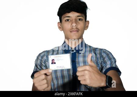 Der indische Schuljunge trägt eine dunkelblaue Schuluniform und zeigt eine verschwommene aadhar-Karte in der Hand. Stockfoto