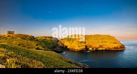 Lange Sonneneinstrahlung des Sonnenlichts in der Nähe der Sommersonnenwende, glühend über Tintagel Haven and Island, Tintagel, Cornwall, Großbritannien Stockfoto