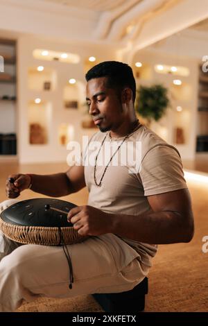 Seitlicher vertikaler Schuss eines schwarzen Schlagzeugers, der in Trance spielt, indem er mit Drumsticks auf Glucophon sitzt und in gemütlicher Meditation im Kreuz auf dem Boden sitzt Stockfoto