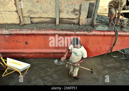 Ein Arbeiter reinigt seine Schaufel, nachdem er Sand von einem Lastkahn entladen hat, während er auf flachem Wasser am Ufer des Musi-Flusses in Süd-Sumatra, Indonesien, steht. Stockfoto