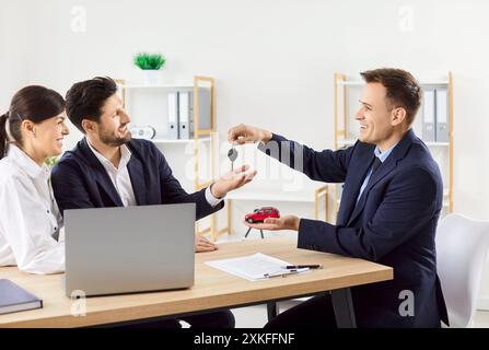 Autoverkäufer im Büro, die Schlüssel an Paare übergeben, Nahaufnahme Stockfoto