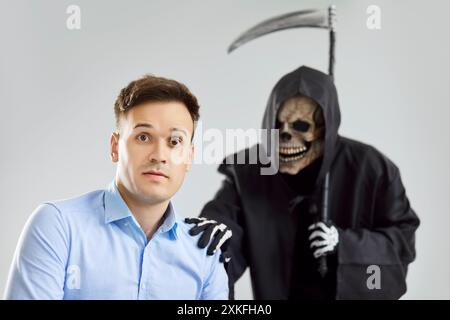 Grimmiger Sensenmann des Todes mit Sensenschulter, der sich an ein neues Opfer anschließt, junger Mann in Todesangst, stirbt Stockfoto