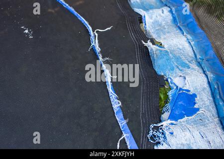 Abgenutzte, veraltete blaue Plane aus Poly-Plane, Federschutz für ein springendes Trampolin, abstrakte, zerlumpte Textur Sicherheitsgefahr Stockfoto