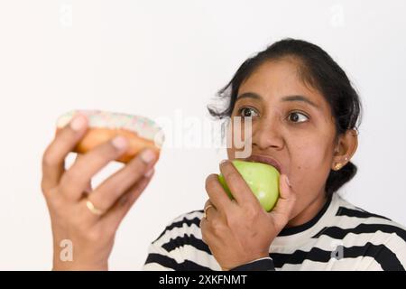 Die Frau hat Schwierigkeiten, zwischen einem süßen Leckerbissen und einem gesunden grünen Apfel zu wählen. Stockfoto