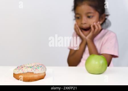 Ein junges Mädchen steht vor einem köstlichen Dilemma und wählt zwischen einer süßen und einer gesunden Option. Stockfoto