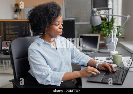 Seitenansicht Porträt einer fokussierten jungen Schwarzen Frau, die als IT-Techniker mit Laptop arbeitet, während sie am Schreibtisch im Softwareentwicklungsbüro sitzt, Kopierraum Stockfoto