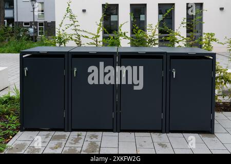 Schwarzer, kompakter, konzeptioneller Stauraum für 4 Mülltonnen im Freien, stehend auf dem Betonboden eines Appartementkomplexes in Deutschland, Frontansicht, Tageslicht. Stockfoto