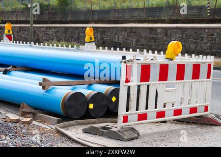 Blaue Wasserrohre auf der Straße an einer neuen Baustelle mit weißen und roten Verkehrszäunen und gelben Lichtern. Die Rohre verlegen sich im Stil eines Neubaus. Stockfoto