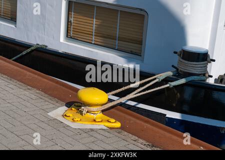 Ein Boot wird an einem Hafen angedockt, gesichert durch Seile, die an einem gelben Schiffspoller befestigt sind. Nahaufnahme. Stockfoto