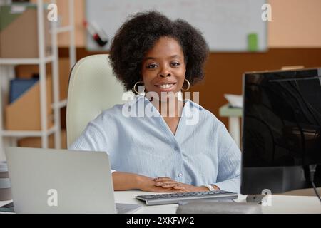 Porträt einer erfolgreichen lächelnden schwarzen Geschäftsfrau, die in die Kamera schaut, während sie im Coworking-Büro mit Computern am Schreibtisch sitzt Stockfoto