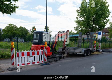 Ein Foto eines Baggers am Straßenrand, daneben befindet sich ein Anhänger mit Schildern und Umzäunungen auf einer Baustelle vor einem Park an einem Sommertag Stockfoto