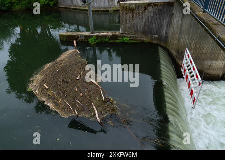 Ein rot-weißes Warnschild hängt über einem kleinen Damm, umgeben von gebrochenem Holz und Ästen, die ins Wasser gefallen sind. Der Bach fließt unter der Brücke. Stockfoto