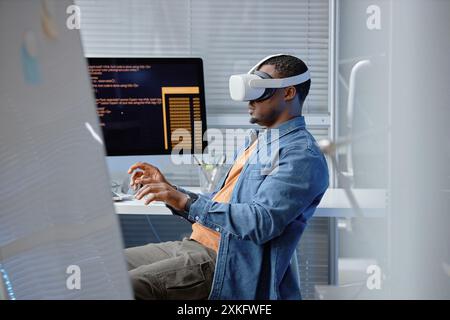 Seitenansicht eines männlichen afroamerikanischen Softwareentwicklers, der die VR-Benutzererfahrung mit VR-Headset im IT-Firmenbüro testet, Kopierraum Stockfoto