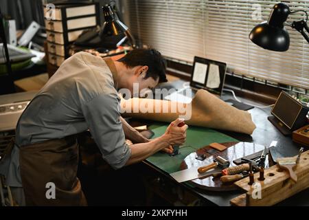 Konzentrierter männlicher Handwerker, der Lederteile am Tisch in seiner Werkstatt schneidet Stockfoto