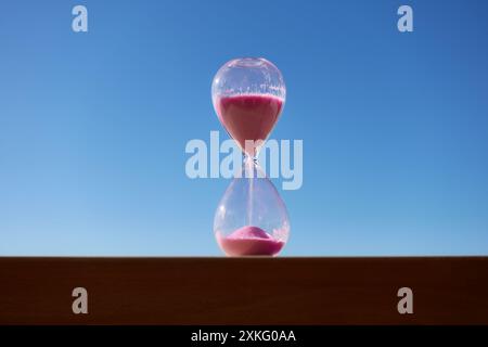 Rosafarbene Sanduhr mit blauem Himmelhintergrund, der den Verlauf der Zeit markiert Stockfoto