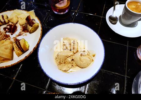 Draufsicht auf Desserts zum Teilen. Weiße Platte mit drei Kugeln Vanilleeis, neben einem Teller mit Feilloas oder Crepes und einem Espresso-Kaffee auf einem Stockfoto