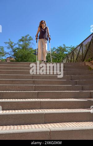 Frau mit Krücken auf der Straße oben auf einer Treppe draußen in einer Stadt Stockfoto