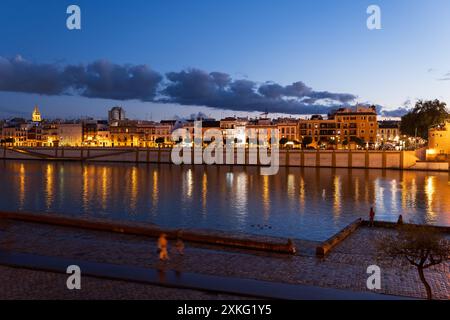 Abend in Sevilla in Andalusien, Spanien. Skyline des Triana-Viertels am Guadalquivir River und an der Uferpromenade. Stockfoto