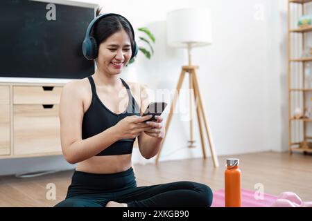 Junge Frau übt Wellness mit Smartphone und Kopfhörern im modernen Wohnzimmer Stockfoto
