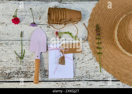 Gartenbaubedarf wie Blumen, Samen, Kelle, Töpfe und ein Strohhut auf rustikalem Holzhintergrund, der die Freude am Pflanzen und Garden repräsentiert Stockfoto