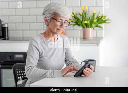 Grauhaarige Attraktive Frau Sucht Nach Informationen Am Telefon Zu Hause Am Tisch Stockfoto