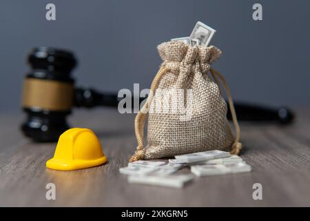 Nahaufnahme eine Tasche mit Geld, Schutzhelm und Hammer auf einem Holztisch. Arbeitnehmerentschädigung, arbeitsrechtliches Konzept. Stockfoto