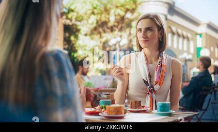 Begeisterte Freundinnen genießen köstliche Desserts in einem gemütlichen City Cafe. Porträt einer schönen jungen Frau, die ein Stück leckeren Schokoladenkuchen probiert, ihre Augen schließt und zufrieden lächelt Stockfoto