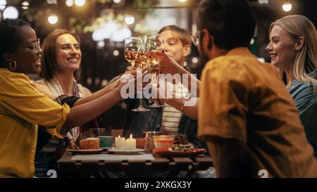 Multiethnische, vielfältige Freunde treffen sich am Abend auf einer Cafe Terrace. Verschiedene junge Menschen, die Gläser mit Wein und Champagner aufziehen, anstoßen und trinken, um ihre Wiedervereinigung zu feiern Stockfoto