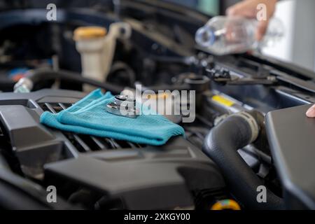 Eine junge Frau füllt den Kühler des Autos mit Wasser und führt eine Fahrzeugwartung durch Stockfoto