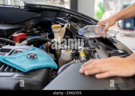 Eine junge Frau füllt den Kühler des Autos mit Wasser und führt eine Fahrzeugwartung durch Stockfoto