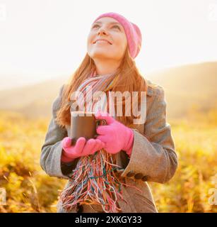 Junge schöne Frau mit Becher in der Hand, die den Herbsthimmel ansieht Stockfoto