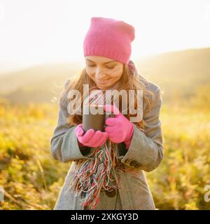 Eine junge Frau, die sich einen Becher in den Händen ansieht und die Herbstsaison genießt Stockfoto