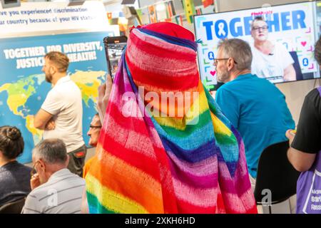 AIDS 2024, Internationale AIDS-Konferenz, Teilnehmer im Veranstaltungsbereich Global Village, Messezentrum, München, Juli 2024 Deutschland, München, 23. Juli 2024, AIDS 2024, 25. Internationale AIDS-Konferenz vom 22. Juli bis 26. Juli. Juli, Teilnehmer mit Regenbogen-Kopftuch an einem Messestand, der sich mit den Themen Diversity, Justice and Health befasst, Teilnehmer berichtet von Diskriminierungen in ihrem jeweiligen Land, Messestand im Global Village, einem Bereich mit Messeständen zu den einzelnen Themen, Messezentrum, Welt-AIDS-Konferenz zum wissenschaftlichen Stand der AIDS-Forschung, zu neue Stockfoto