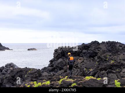 Mann im Coasteering-Anzug, der entlang der schwarzen vulkanischen Klippen auf der Insel Sao Miguel auf den Azoren läuft Stockfoto