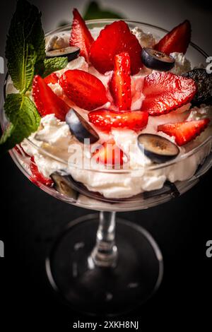 Erdbeerdessert mit Heidelbeeren, Mascarpone und Schlagsahne, frische Erdbeeren in einem Glas mit Quark auf schwarzem Hintergrund. Rezept für A Stockfoto