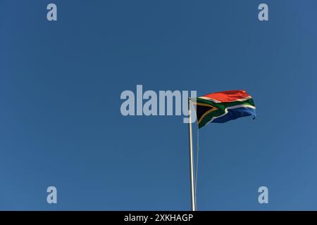 Die südafrikanische Flagge auf einem Fahnenmast, die an einem sonnigen Tag im Wind winkt. Stockfoto