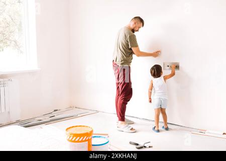 Renovierung des Apartments. Der kleine Junge hilft seinem Vater, an die Wände zu gehen. Ein junger Mann in legeren Klamotten mit süßem Sohn repariert im Zimmer. Vater und Kind A Stockfoto