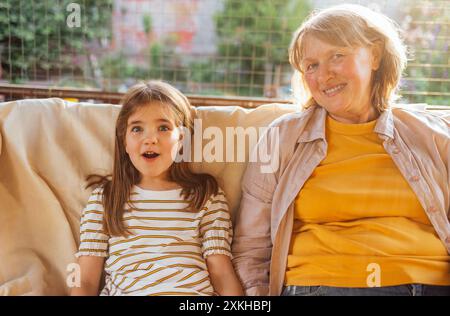 Lächelnde reife Frau und ihre süße Enkelin im Hinterhof des Hauses. Lachende Großmutter umarmt ihre kleine Enkelin. Rentner und Kind sind rel Stockfoto