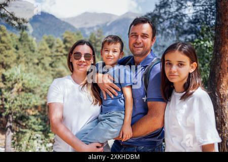 Glückliche Familie auf dem Hintergrund der Berglandschaft. Junge verheiratete Paare mit ihrem Sohn und ihrer Tochter laufen im Wald. Lächelnde Touristen genießen Natur Stockfoto