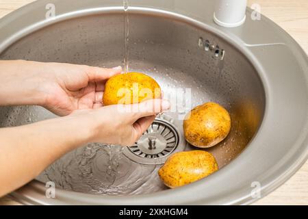 Die Hausfrau wäscht frische Kartoffeln in der Küchenspüle. Stockfoto